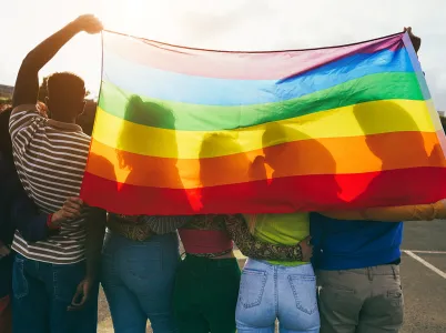 Four people draping an LGBTQ+ flag over their shoulders.
