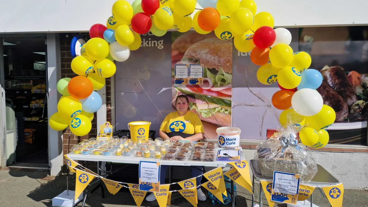 A F Blakemore staff member behind a cake stall raising money for Marie Curie outside a SPAR convenience store.